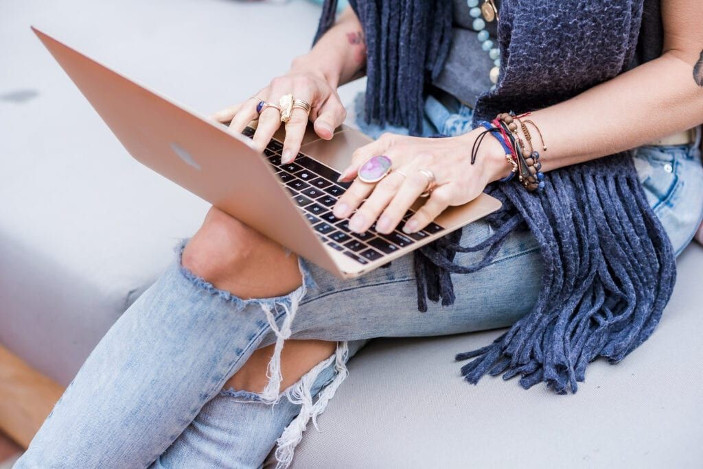 Woman wearing jewelry, scarf and worn jeans typing on a computer