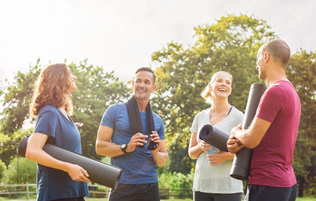 Group of adults holding exercise mats gathered in a park for a workout