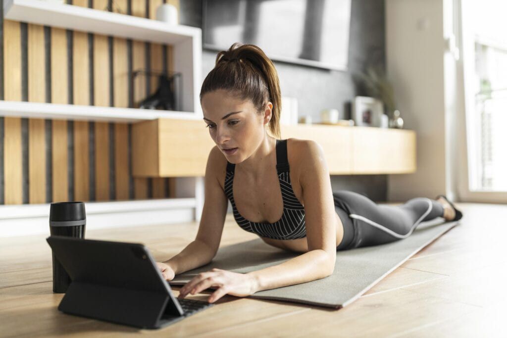Woman lying on Pilates mat while typing on her tablet
