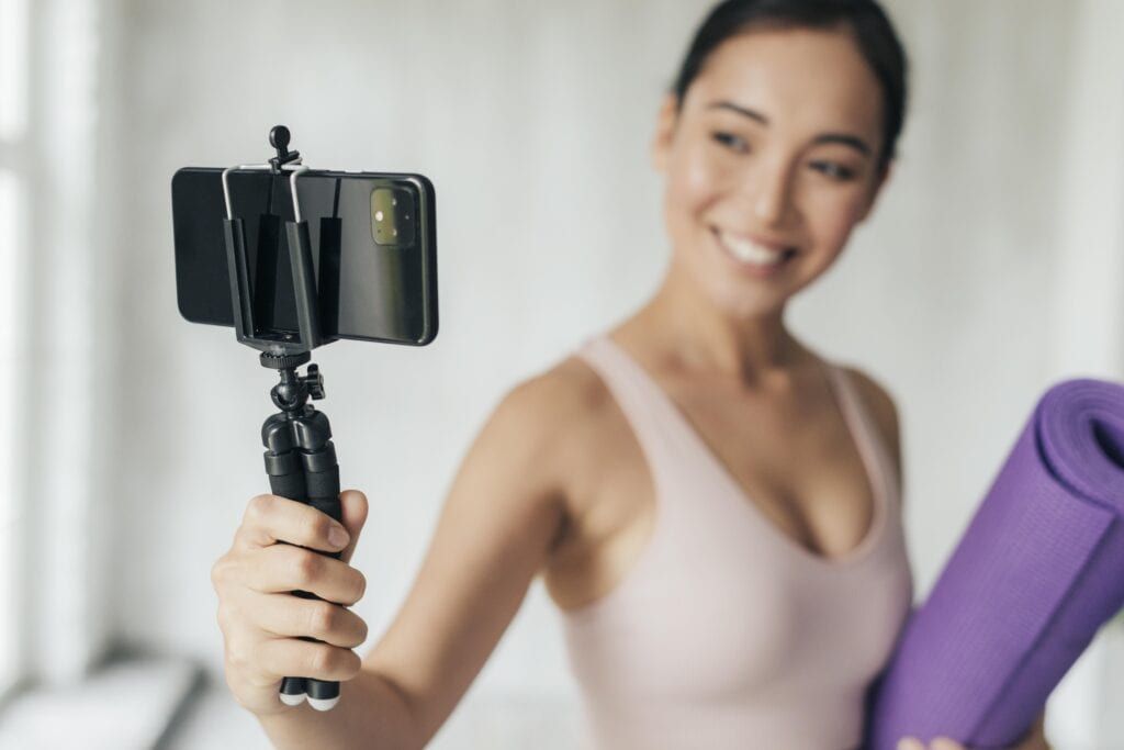 Smiling woman vlogging with her phone and Pilates mat