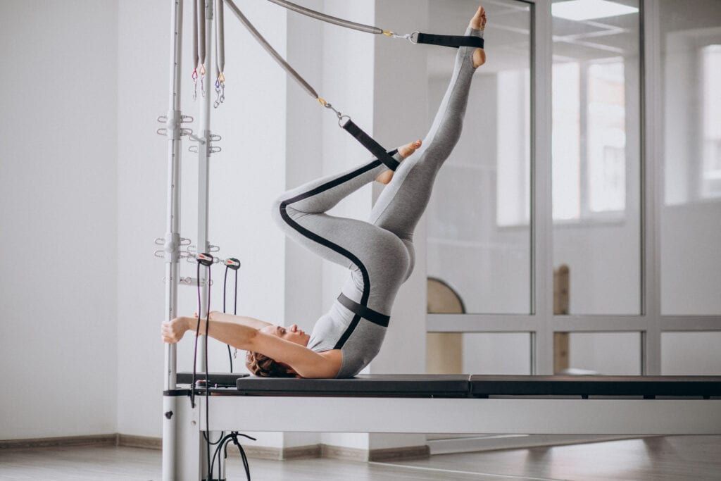 Woman wearing athletic clothing exercising on Pilates reformer in studio