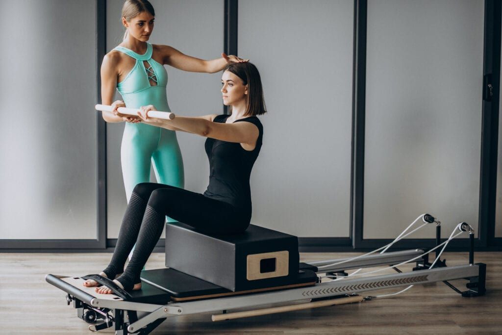 Pilates Instructor helping student on reformer